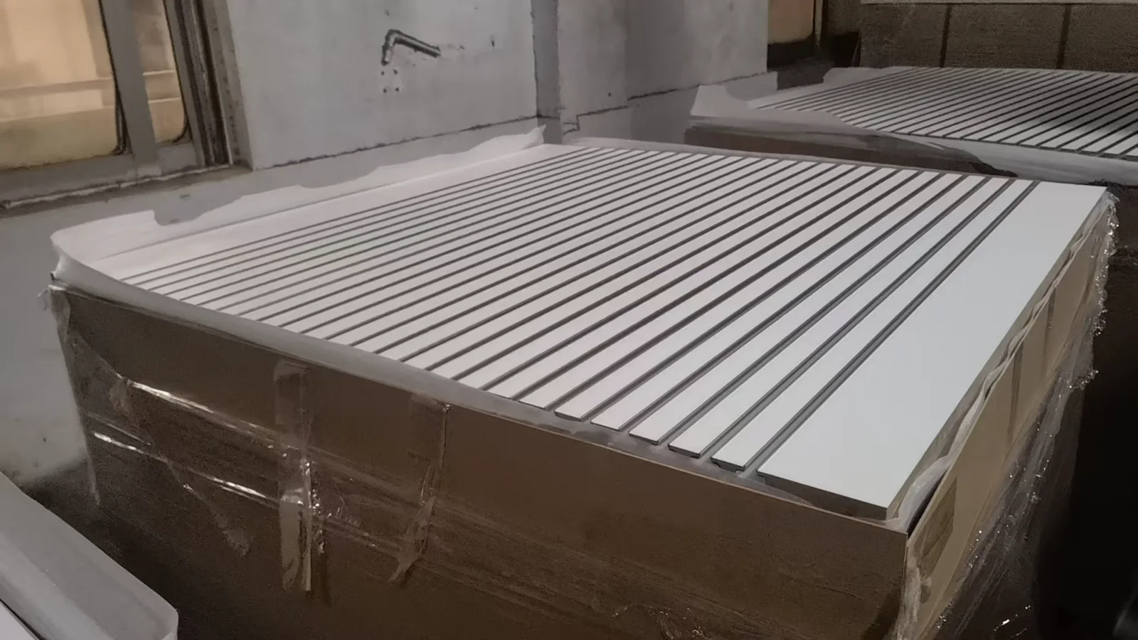 Finished white MDF slatwall panels with dark inserts stacked for protection